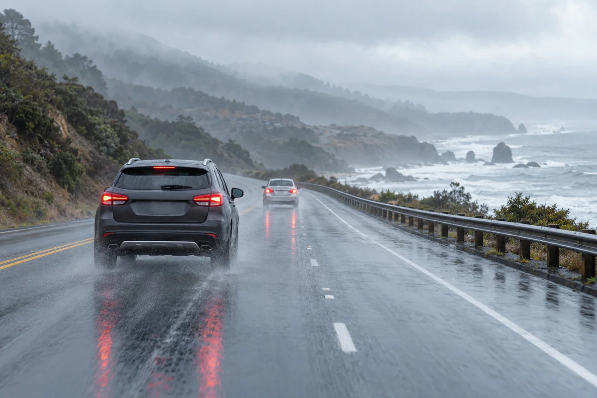 Cars travel cautiously with ample following distance on a wet California coastal road.