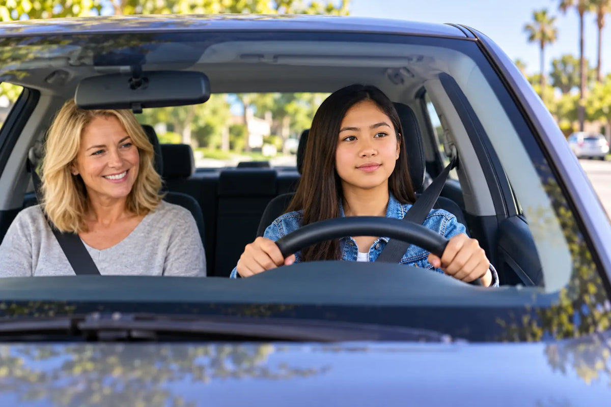 A teen practices driving with an adult supervisor on a California neighborhood street.